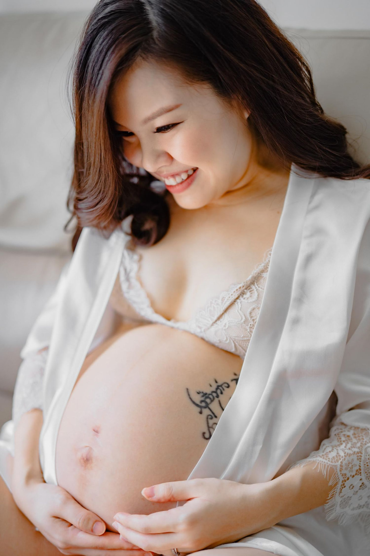 Vivian Ho — smiling portrait in a white robe, hands cradling the bump