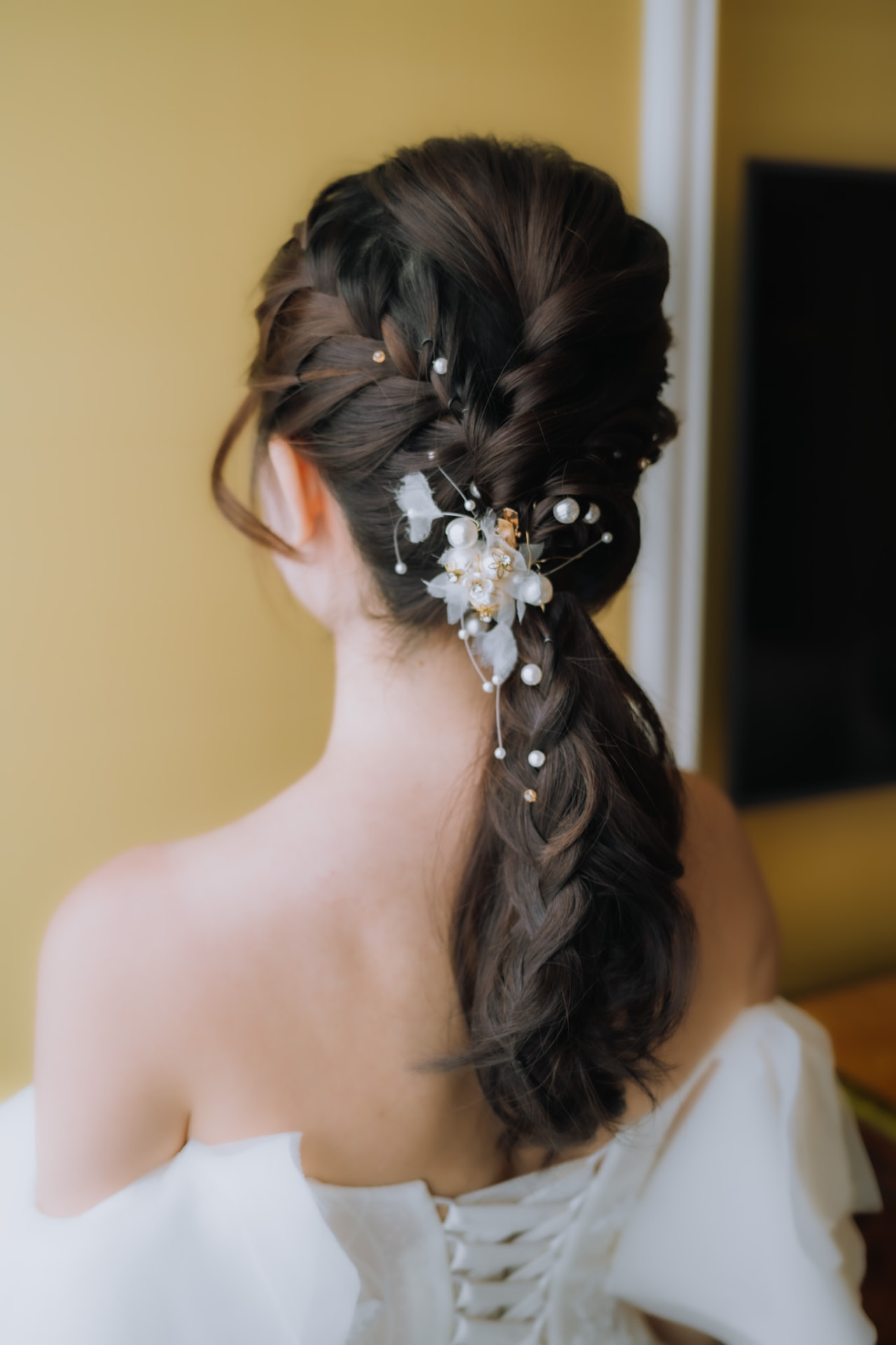 Bride's braided ponytail scattered with pearls, from behind