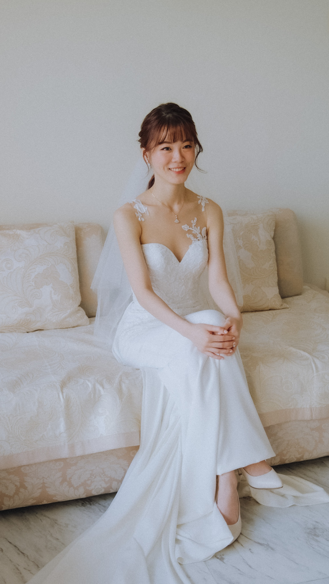 Bride smiling, seated in her gown with a low ponytail