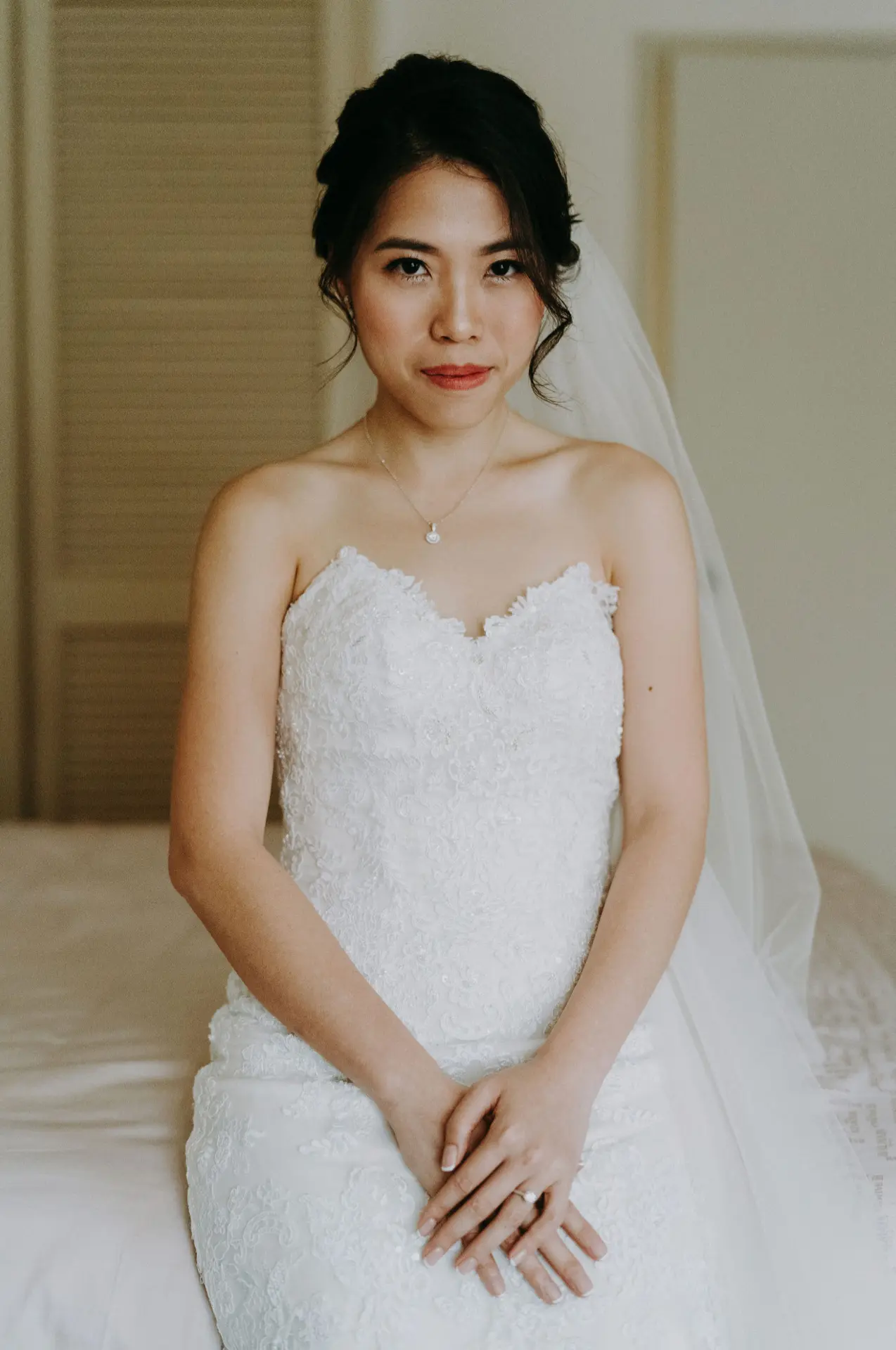 Bride seated in her lace gown and veil, hands resting together