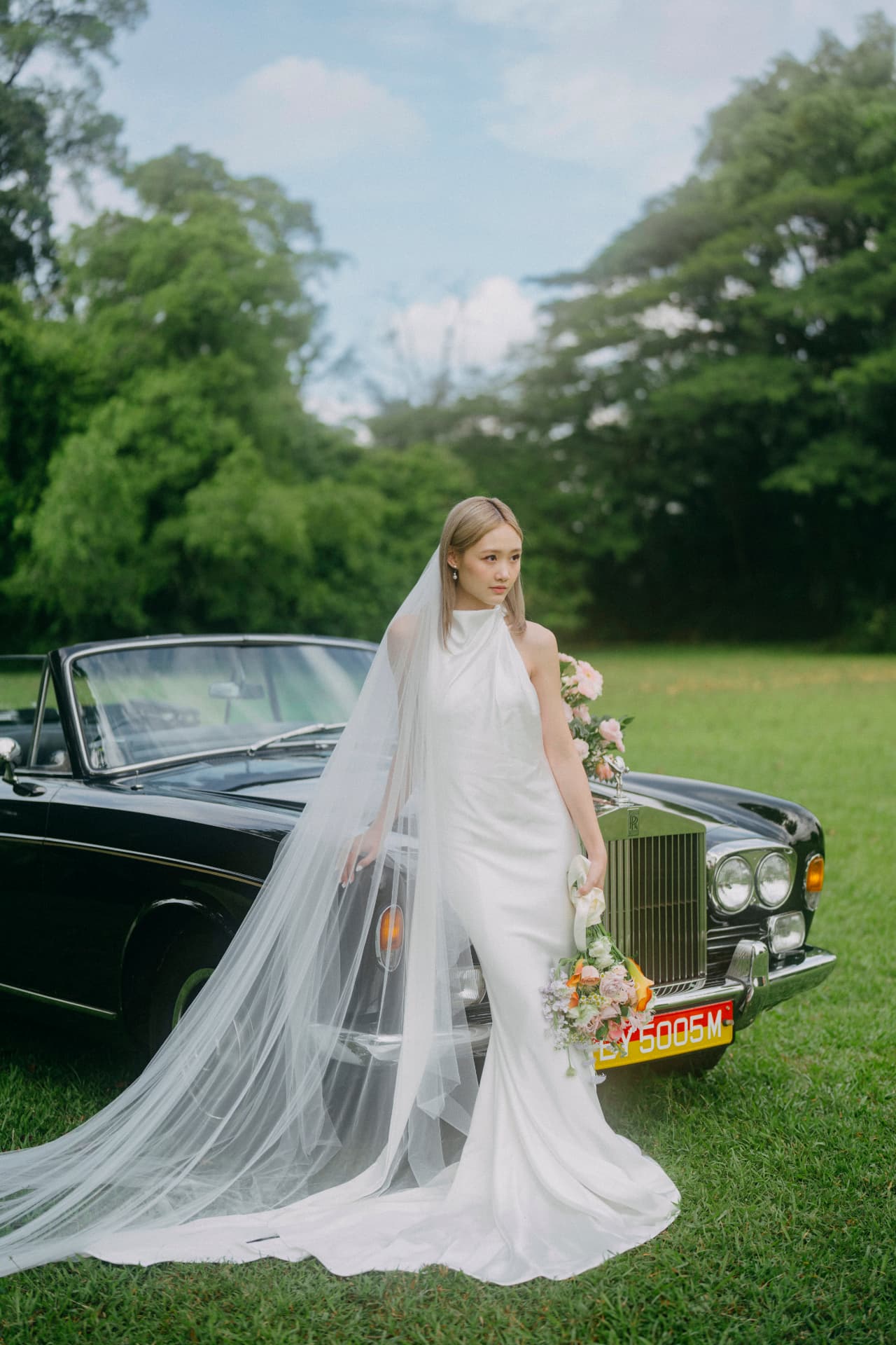 Denise — full gown and long veil beside the car