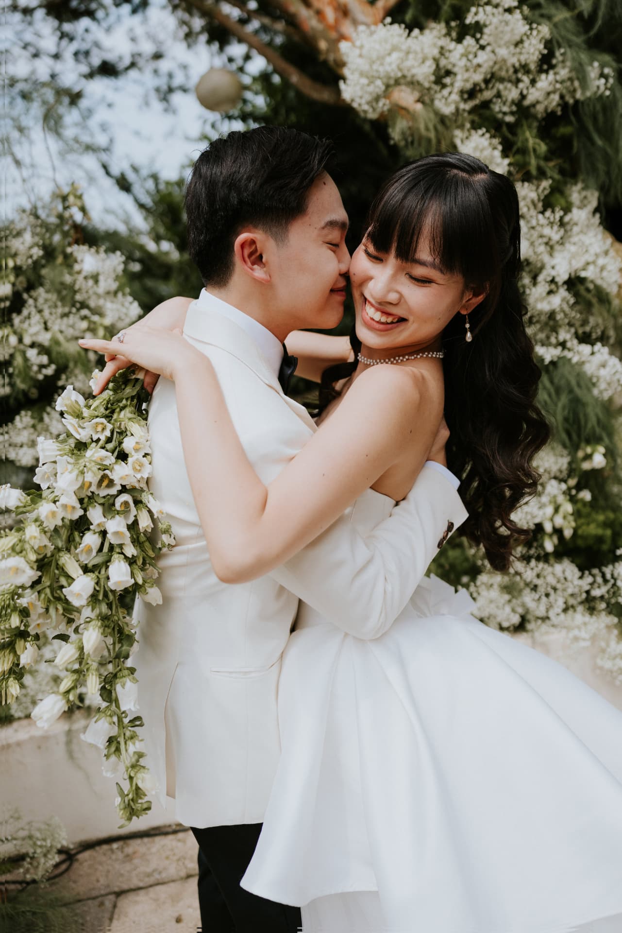 Cloud Dancer — the groom kissing the bride's cheek as she laughs, bellflower bouquet