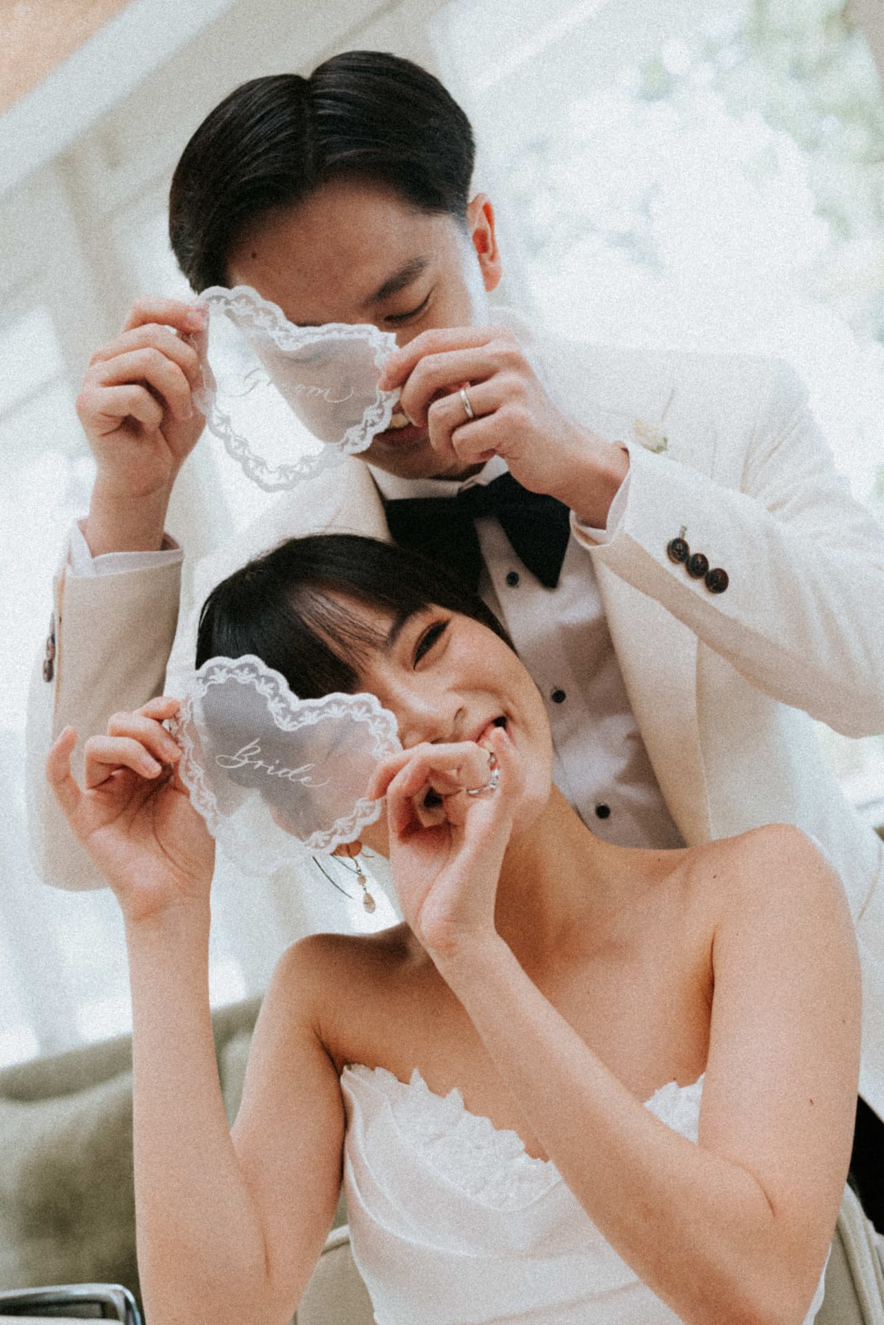 Cloud Dancer — the couple laughing behind the lace Groom and Bride doilies