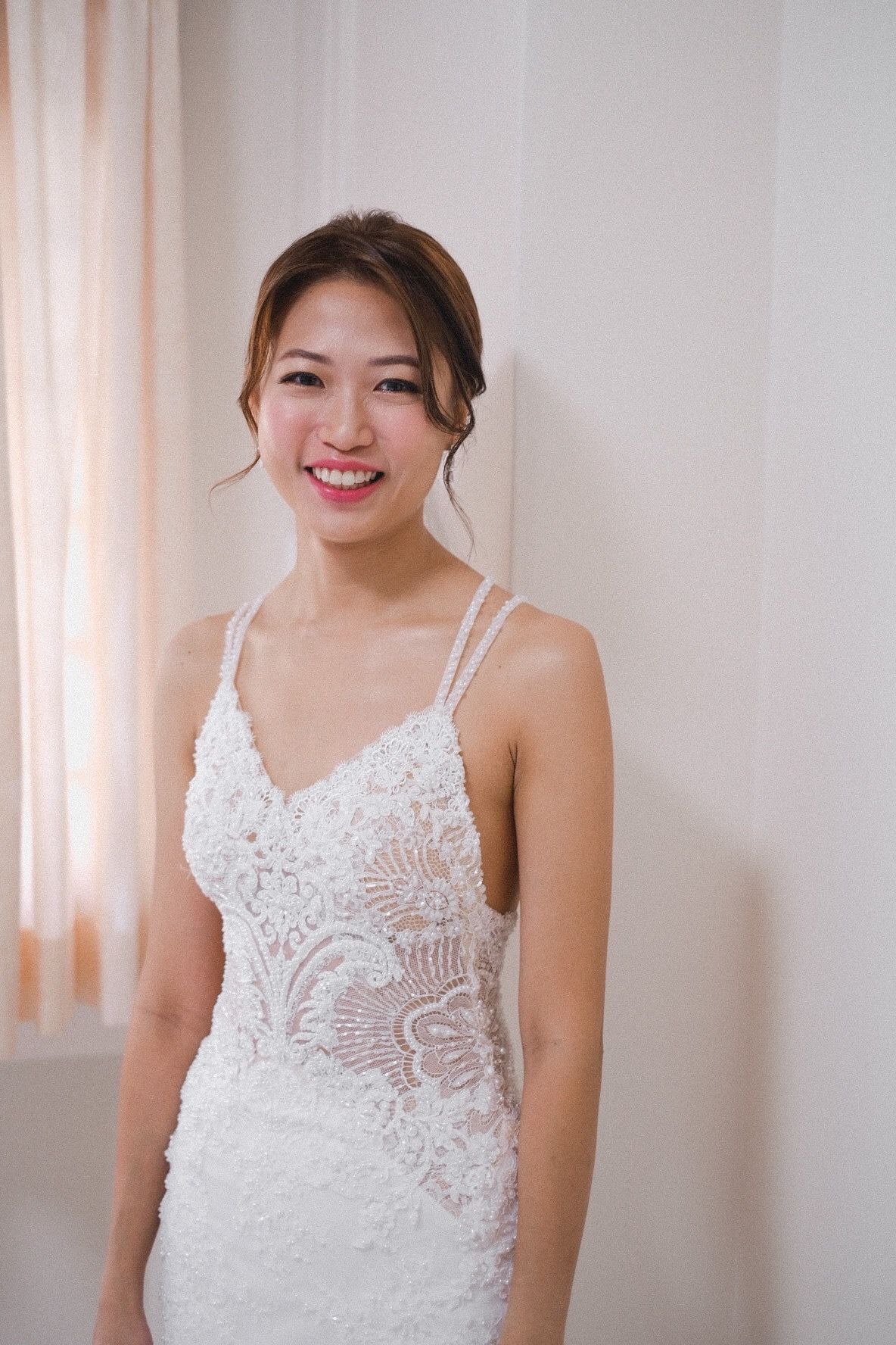 Bride smiling in her beaded lace gown by the window light