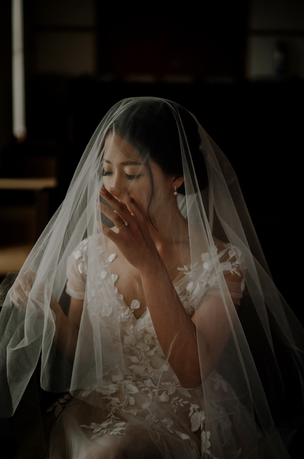 Bride lifting a hand to her face beneath the veil