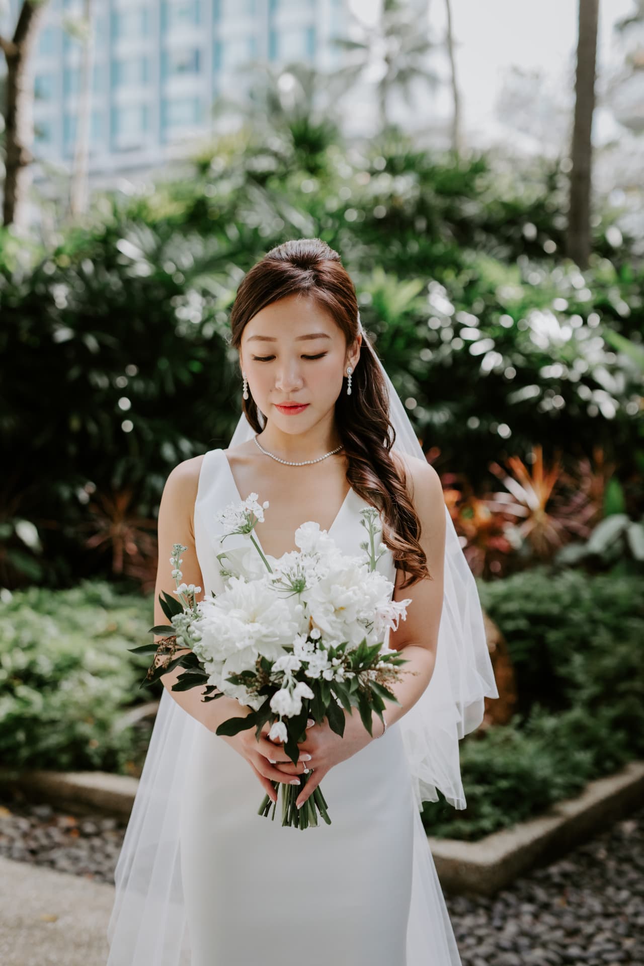 Bride in the garden holding her white bouquet, eyes lowered